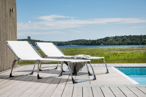 Zwei AMIGO XXL Dreibeinliegen mit weißer Textilene-Liegefläche und silbernem Aluminium-Gestell nebeneinander am Pool.