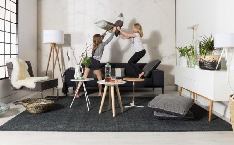 Beistelltisch CORONA aus massiver Eiche in Naturholz-Optik, Gesamtansicht in Wohnzimmer-Szenerie neben schwarzem Sofa.