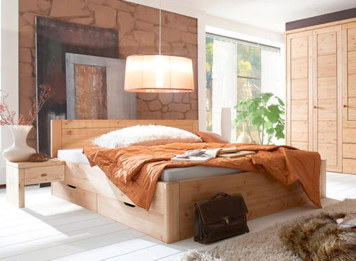 Massivholzbett VITA XL 200 x 200 mit ausfahrbaren Schubladen in Gesamtansicht im hellen Schlafzimmer mit Kiefer-Kopfteil.