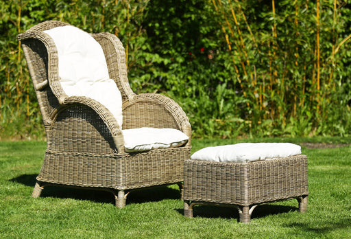 Relax Rattan Ohrensessel CONSUL mit Fußhocker in Gesamtansicht von vorne, beide Teile mit weißen Polstern auf Rasen.