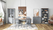 Kommode LUZERNA 3.1 mit zwei Glastüren in grauer Ausführung, in Wohnzimmerambiente mit Esstisch und Regalen platziert.