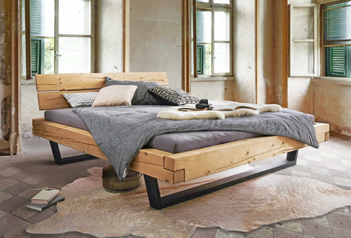 Balkenbett GORM mit Metallkufen aus Fichte in Gesamtansicht mit grauer Bettwäsche und Kissen, schwarze Metallkufen sichtbar.