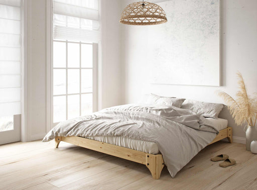 Futonbett ELAN Massivholzbett Gestell Kiefer natur in Gesamtansicht mit grauer Bettwäsche in hellem Schlafzimmer.