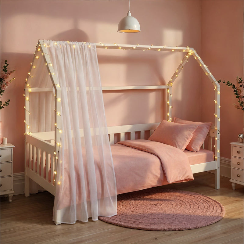 Kinderbett FUNKY HOUSEBED 90 x 200 weiß in Gesamtansicht mit Himmelgestell, weißem Vorhang und Lichterkette.
