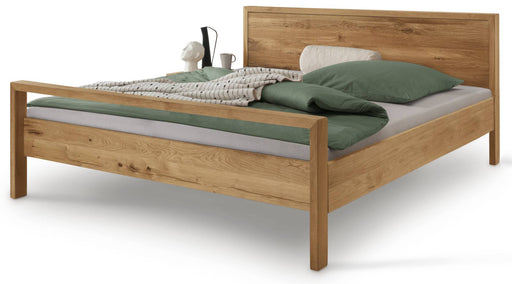 Massivholzbett AAGE 1 Holzbett Wildeiche geölt mit hochwertigem Kopfteil, eingedeckt mit grüner Bettwäsche und Kissen.