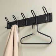Schwarze Wandgarderobe mit fünf Doppelhacken, an der ein beigefarbenes Handtuch und ein Kleiderbügel hängen