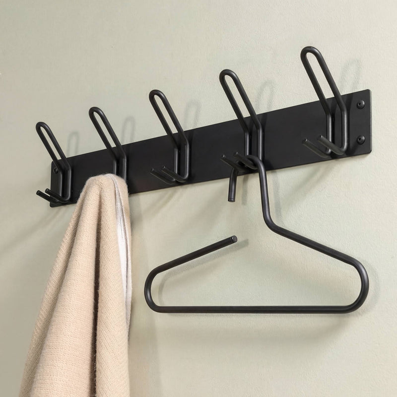 Schwarze Wandgarderobe mit fünf Doppelhacken, an der ein beigefarbenes Handtuch und ein Kleiderbügel hängen
