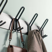 Schwarze Garderobenleiste mit Haken, an denen eine braune Tasche und ein brauner Mantel hängen
