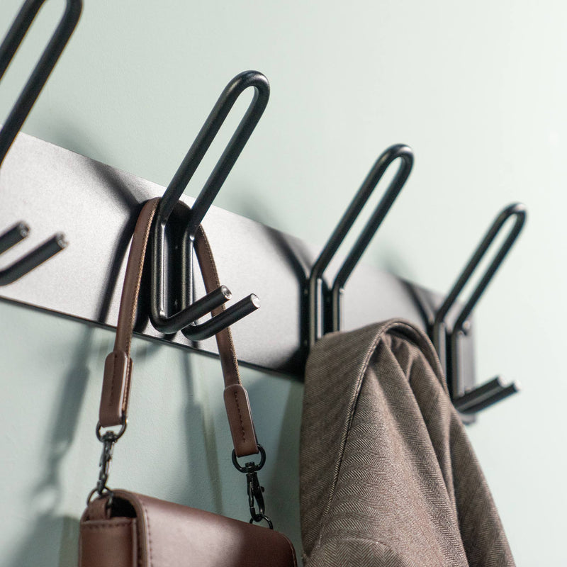 Schwarze Garderobenleiste mit Haken, an denen eine braune Tasche und ein brauner Mantel hängen