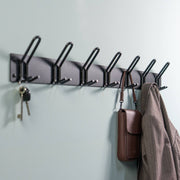 Schwarze Wandgarderobe mit sechs Haken, an denen Schlüssel, eine braune Tasche und eine Jacke hängen