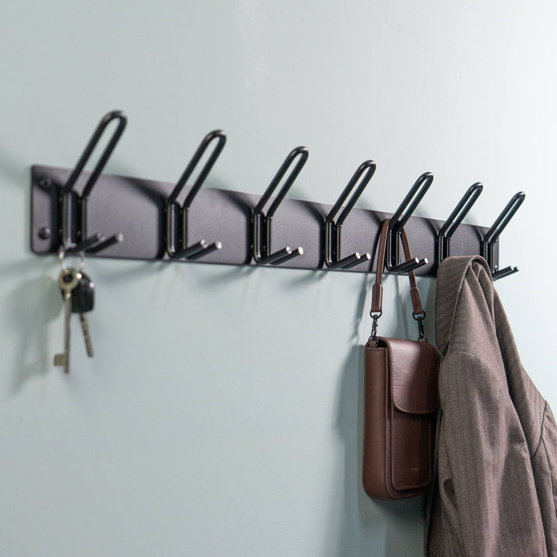 Schwarze Wandgarderobe mit sechs Haken, an denen Schlüssel, eine braune Tasche und eine Jacke hängen