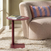 Roter Beistelltisch mit Buch neben beigem Sofa und gestreiftem Kissen auf flauschigem Teppich