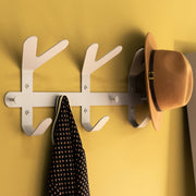Hut und Hemd hängen an einem weißen Wandhaken vor einer gelben Wand