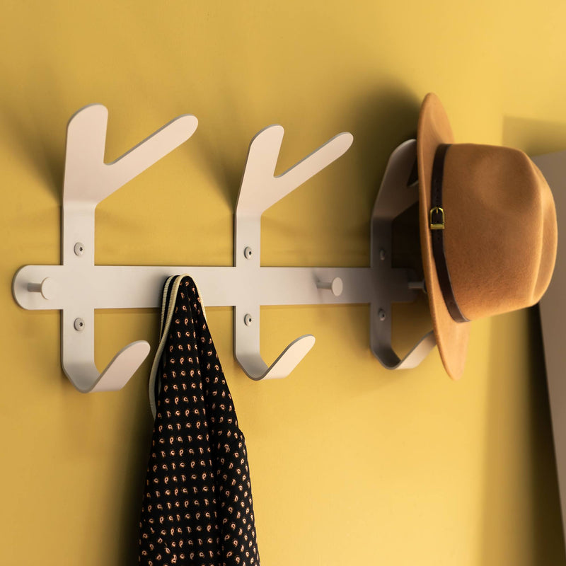Hut und Hemd hängen an einem weißen Wandhaken vor einer gelben Wand
