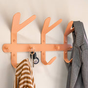 Lachsfarbene Garderobe mit drei Haken und drei Knöpfen, an der ein gestreiftes Hemd, Schlüssel und eine Jacke hängen