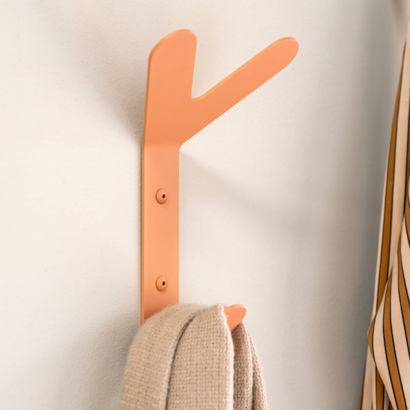 Korallfarbener Wandhaken mit zwei Ästen, an dem ein beigefarbener Strickschal hängt