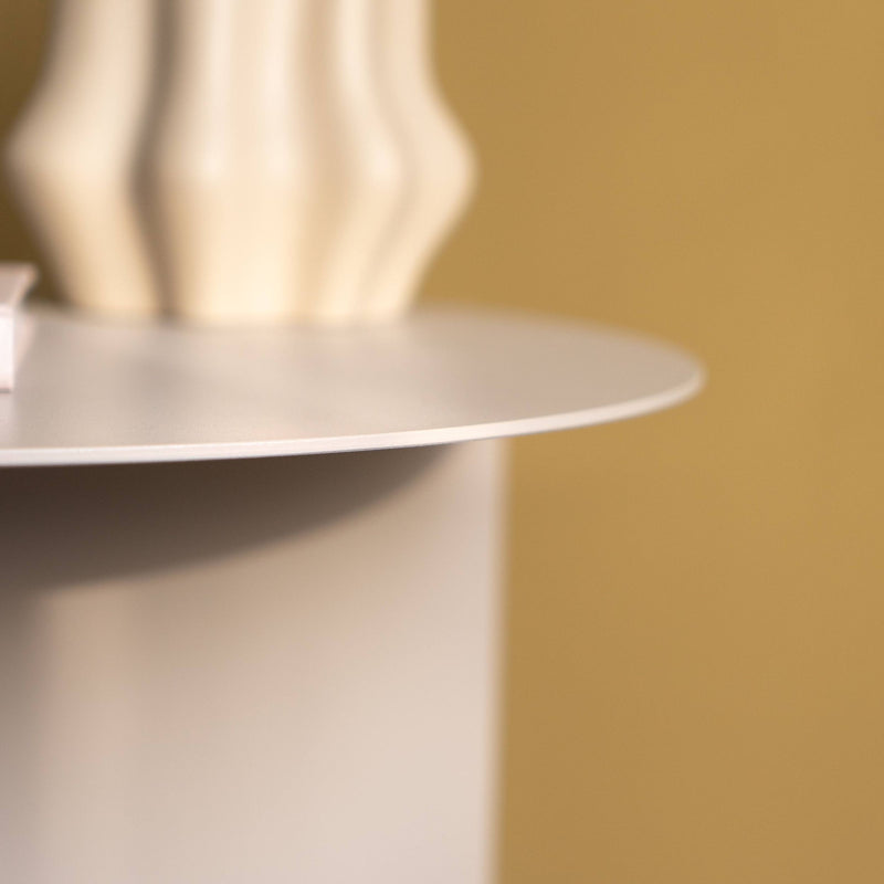 Beige Vase auf einem runden Beistelltisch vor einer senfgelben Wand