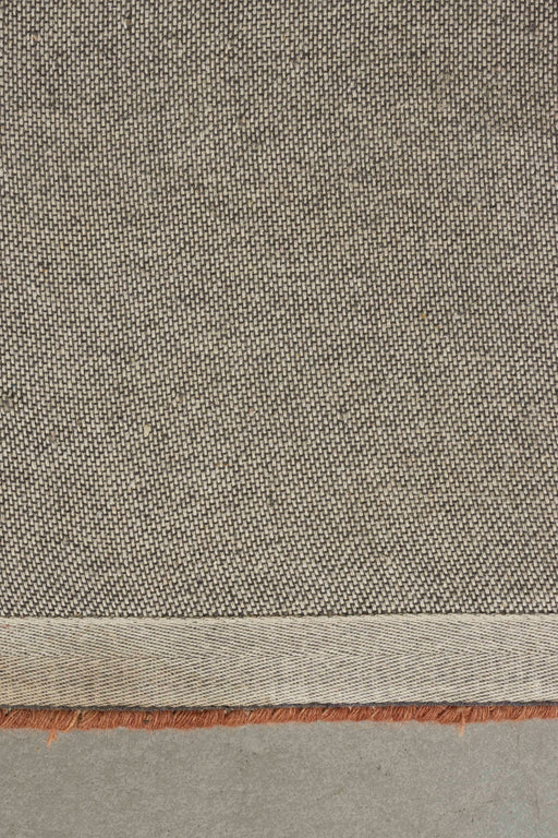 Teppich Maryland Rust 160x230 cm mit graubeigem Flachgewebe und rostrotem Streifendetail an der Kante.