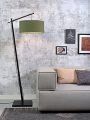 Good&Mojo Stehleuchte Andes mit schwarzem Bambusgestell und waldgrünem Stoffschirm in einem Wohnzimmer neben einem Sofa.