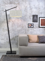 Stehleuchte Andes mit schwarzem Bambusgestell und hellem Leinenschirm in Wohnzimmer-Ambiente neben einem grauen Sofa.