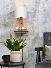 Wandleuchte Andes von Good&Mojo mit weißem Leinenschirm und Bambusgestell, an der Wand mit Ablage und Büchern.