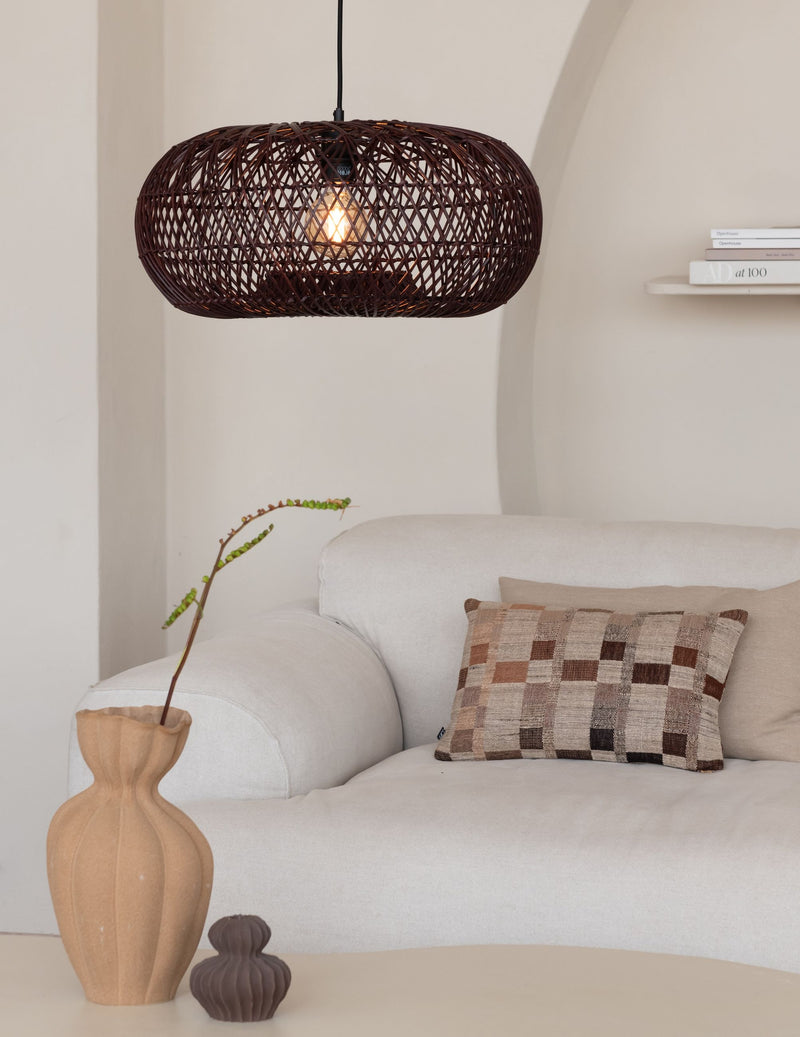 Weinrote Hängeleuchte Arizona aus geflochtenem Rattan über einem hellen Sofa mit Zierkissen.
