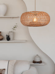 Hängeleuchte Arizona aus geflochtenem Rattan in Naturfarbe, über einem hellen Sofa in einem weiß gestalteten Wohnraum.