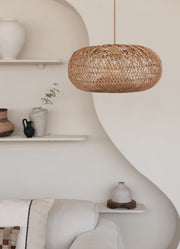 Hängeleuchte Arizona aus Rattan in Natur, im Wohnraum vor einer geschwungenen Wand mit weißen Wandregalen.
