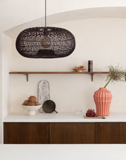 Gesamtansicht der Hängeleuchte Arizona aus dunkelbraunem Rattan über einem Sideboard mit Holzfronten und weißer Platte.