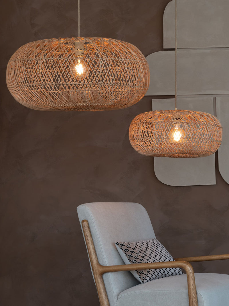 Zwei ovale Hängeleuchten aus geflochtenem Naturrattan über einem grauen Sessel mit Holzgestell vor dunkler Wand.