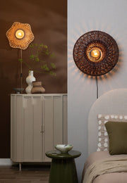 Runde Wandleuchte Arizona mit dunkel geflochtenem Rattanschirm und Eisengestell, an heller Wand über einem Bett, Ø 50 cm.