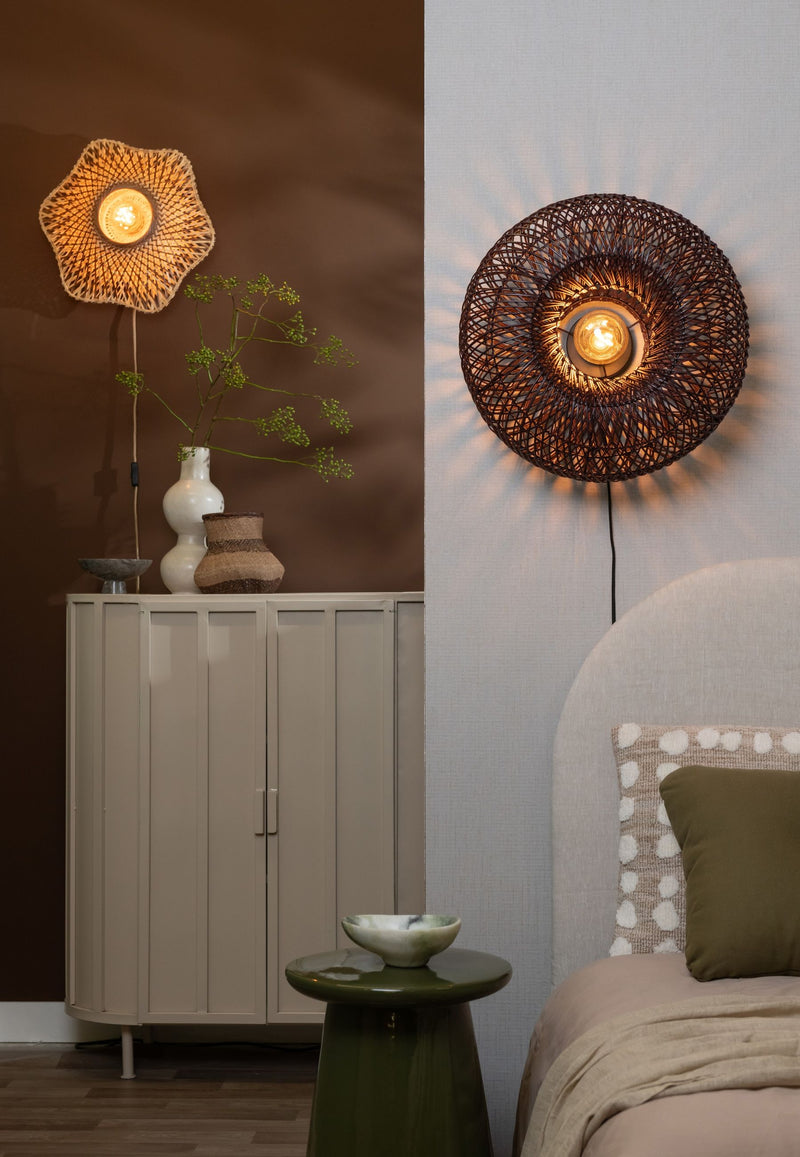 Runde Wandleuchte Arizona mit dunkel geflochtenem Rattanschirm und Eisengestell, an heller Wand über einem Bett, Ø 50 cm.