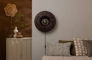Good&Mojo Wandleuchte Arizona in Weinrot: runder Rattanschirm mit dunklem Geflecht, an einer hellen Wand über einem Sofa.