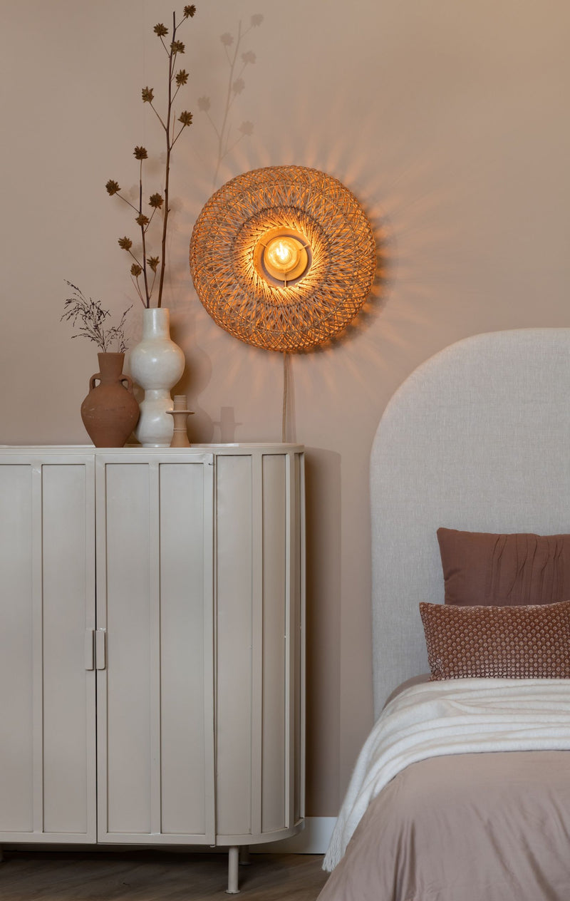 Runde Wandleuchte Arizona aus natürlichem Rattan mit leuchtender Glühbirne, montiert über einem Sideboard im Schlafzimmer.