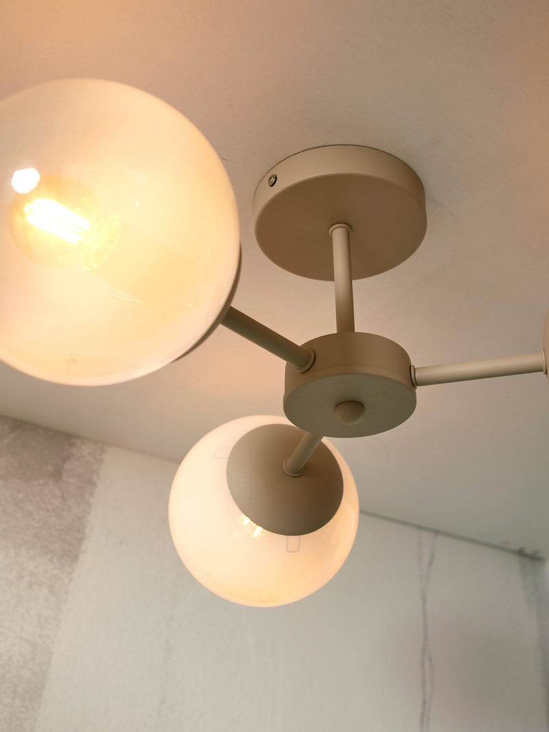 Deckenleuchte „It's about RoMi Aspen“ mit drei runden Glasschirmen an beige lackierten Metallarmen, Ansicht von unten.