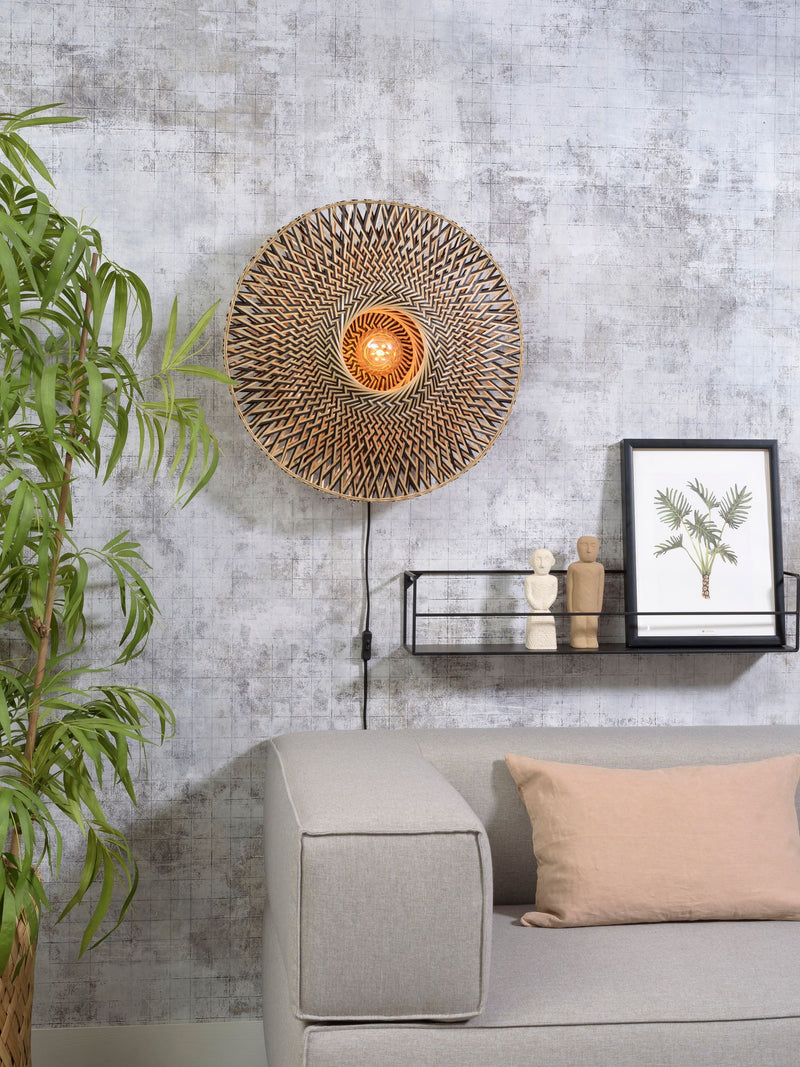 Gesamtansicht der Wandleuchte Bali von Good&Mojo aus Bambus in Natur/Schwarz, mit Leuchtmittel an der Wand über dem Sofa.