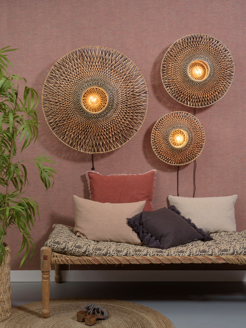 Drei runde Wandleuchten Bali aus Bambus in Natur/Schwarz mit geflochtenem Muster über einer Sitzbank an einer rosa Wand.