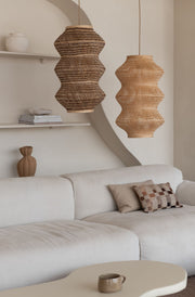Zwei geflochtene Hängeleuchten Barbados XL aus Bambus mit wellenförmiger Silhouette über einem hellen Sofa im Wohnzimmer.