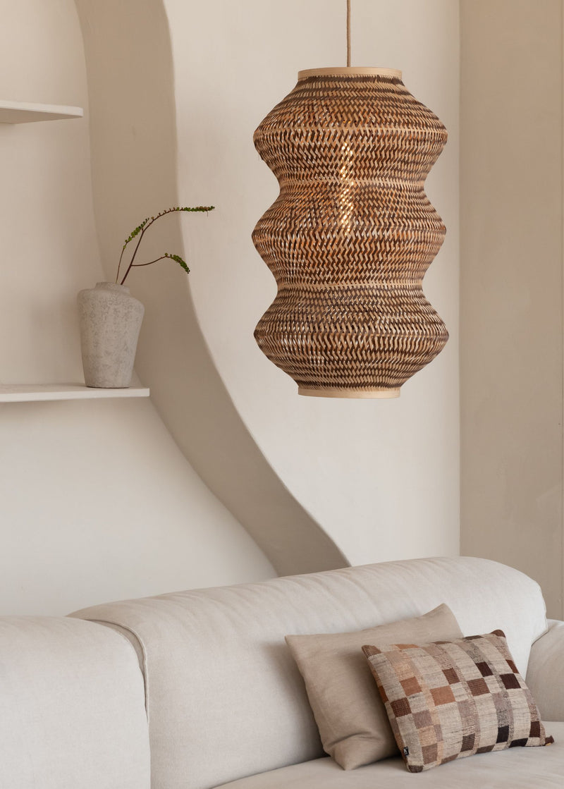 Hängeleuchte Barbados XL von Good&Mojo mit geschwungenem Bambusschirm in Erdtönen, im Wohnraum über einem hellen Sofa.