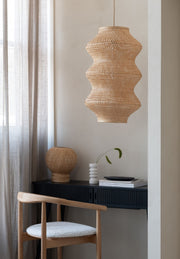 Hängeleuchte Barbados XL von Good&Mojo aus geflochtenem Bambus mit wellenförmigem Schirm über einem schwarzen Sideboard.