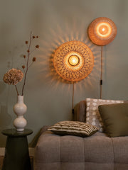 Wandleuchte Barbados von Good&Mojo mit rundem Bambusschirm in Natur, über einem Sofa an der Wand, warm beleuchtet.