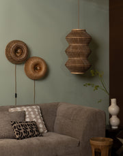 Zwei runde Wandleuchten Barbados mit Bambusschirmen an einer grünen Wand, daneben Sofa und Vase.