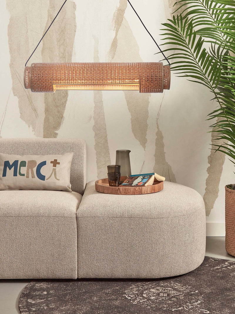 Hängeleuchte Bhutan aus Bambus in Naturfarbe über einem beigen Sofa mit Holztablett und Palmenpflanze.