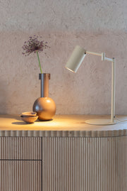 Tischleuchte RoMi Bilbao in Beige mit verstellbarem Eisenschirm auf einer Anrichte neben einer Vase mit Zierlauch.