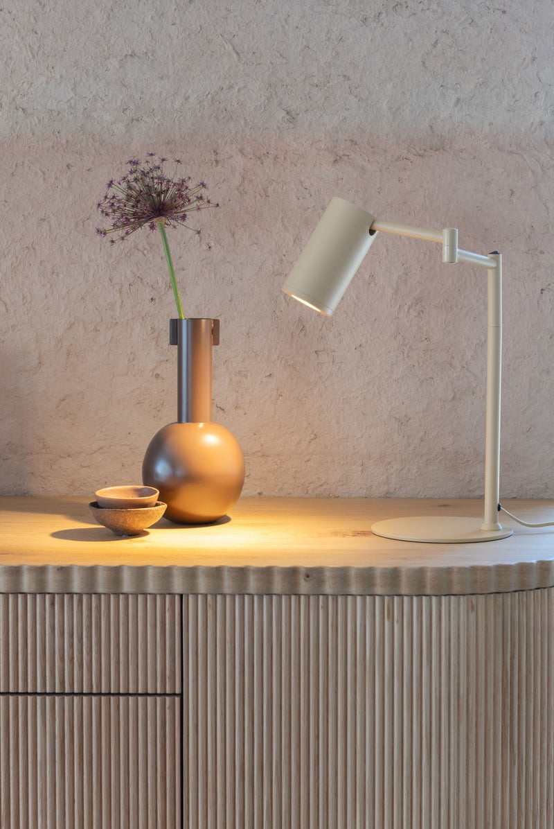 Tischleuchte RoMi Bilbao in Beige mit verstellbarem Eisenschirm auf einer Anrichte neben einer Vase mit Zierlauch.