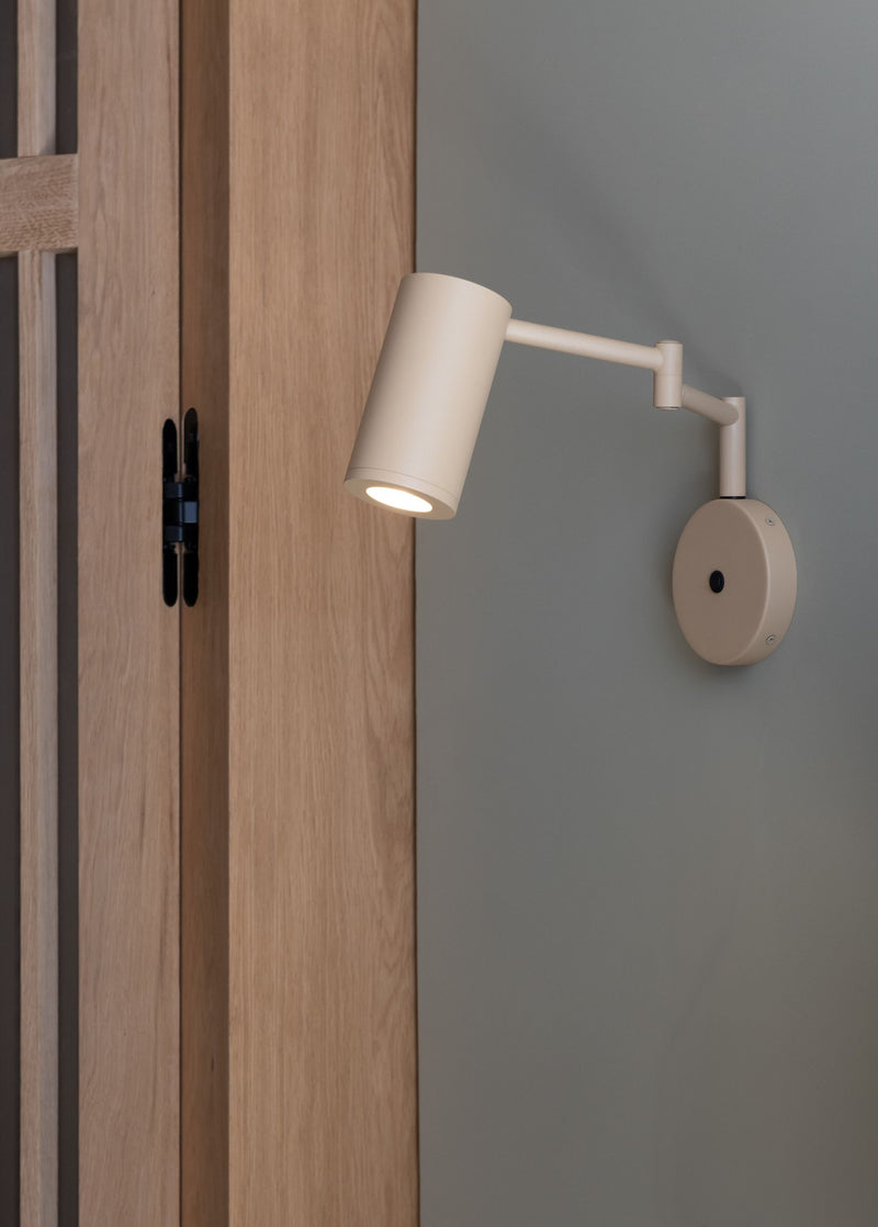 It’s about RoMi Wandleuchte Bilbao in Beige: Eisen-Wandleuchte mit schwenkbarem Arm und zylindrischem Schirm vor grauer Wand