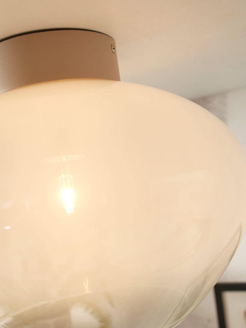 Detailansicht der Deckenleuchte It's about RoMi Bologna mit milchweißem Glasschirm, metallischem Befestigungsteller und sichtbarer Glühlampe.