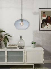 Gesamtansicht der Hängeleuchte Bologna mit blau-grauem Glasschirm über einem weißen Sideboard mit Glasvase.