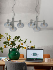 Hängeleuchte It's about RoMi Bologna mit vier grauen Glasschirmen über einem Holztisch mit Laptop und grüner Vase.
