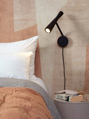 Die Wandleuchte RoMi aus Eisen in Schwarz mit verstellbarem Arm und Schalter neben dem Bett.